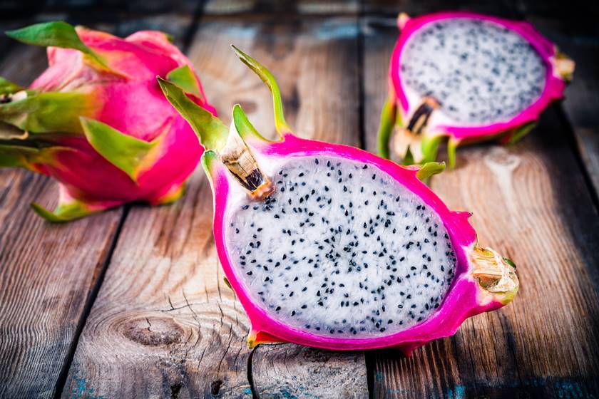 Foto colorida. Fruta rosa na parte externa e branca com sementes pretas no seu interior - Metrópoles