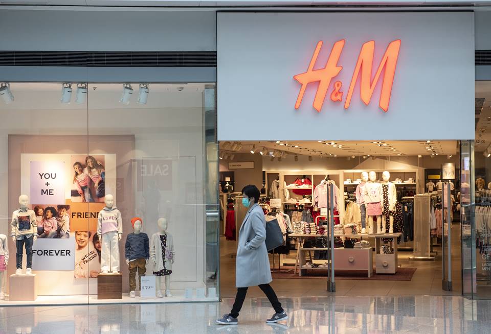 Mulher passando de máscara cirúrgica na frente de uma loja da H&M