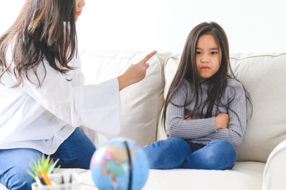 Mãe brigando com menina que reage com cara de raiva