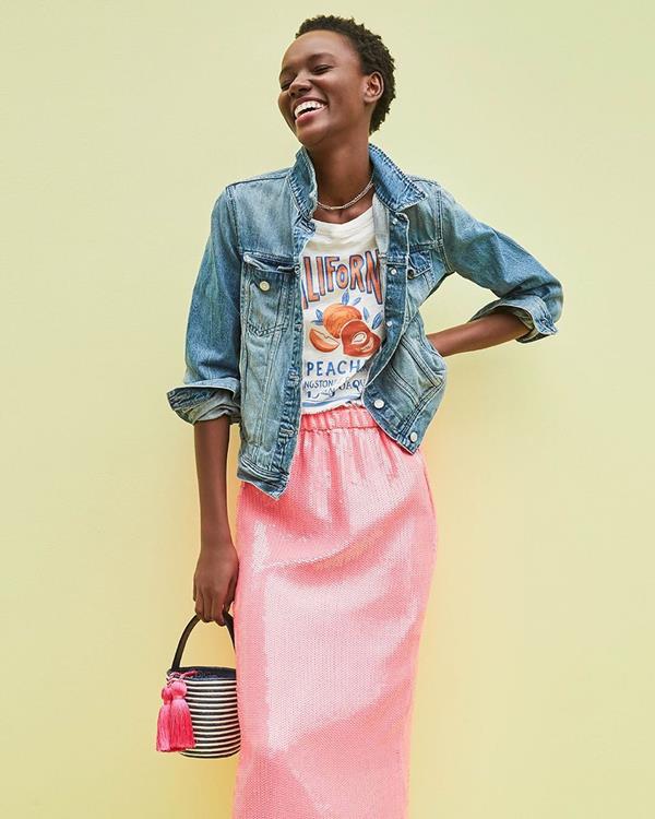 Modelo com jaqueta, camiseta, saia rosa e bolsa em foto da marca J.Crew