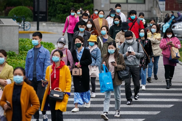 Na China, pessoas atravessam a rua usando máscara