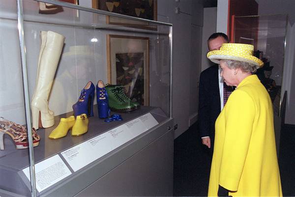 Rainha Elizabeth II no museu Victoria & Albert vendo o sapato Vivienne Westwood que derrubou Naomi Campbell em 1993