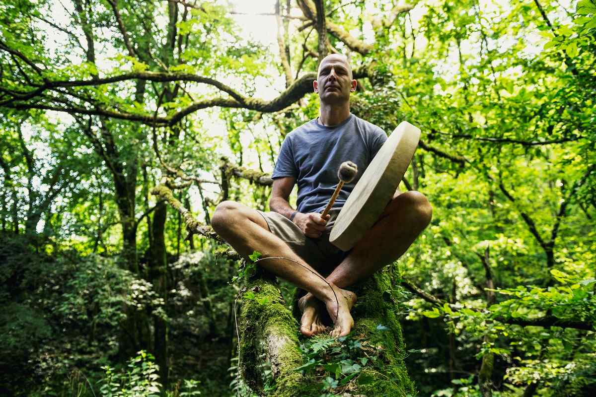 homem segura instrumento sentado em pedra em meio à natureza