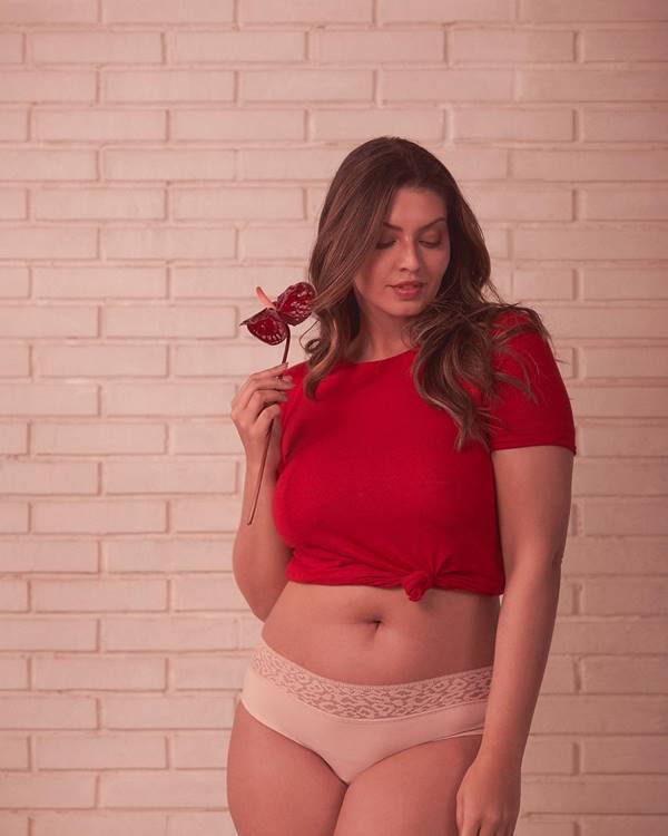 Modelo usando calcinha absorvente rosa, com blusa vermelha, e segurando uma flor