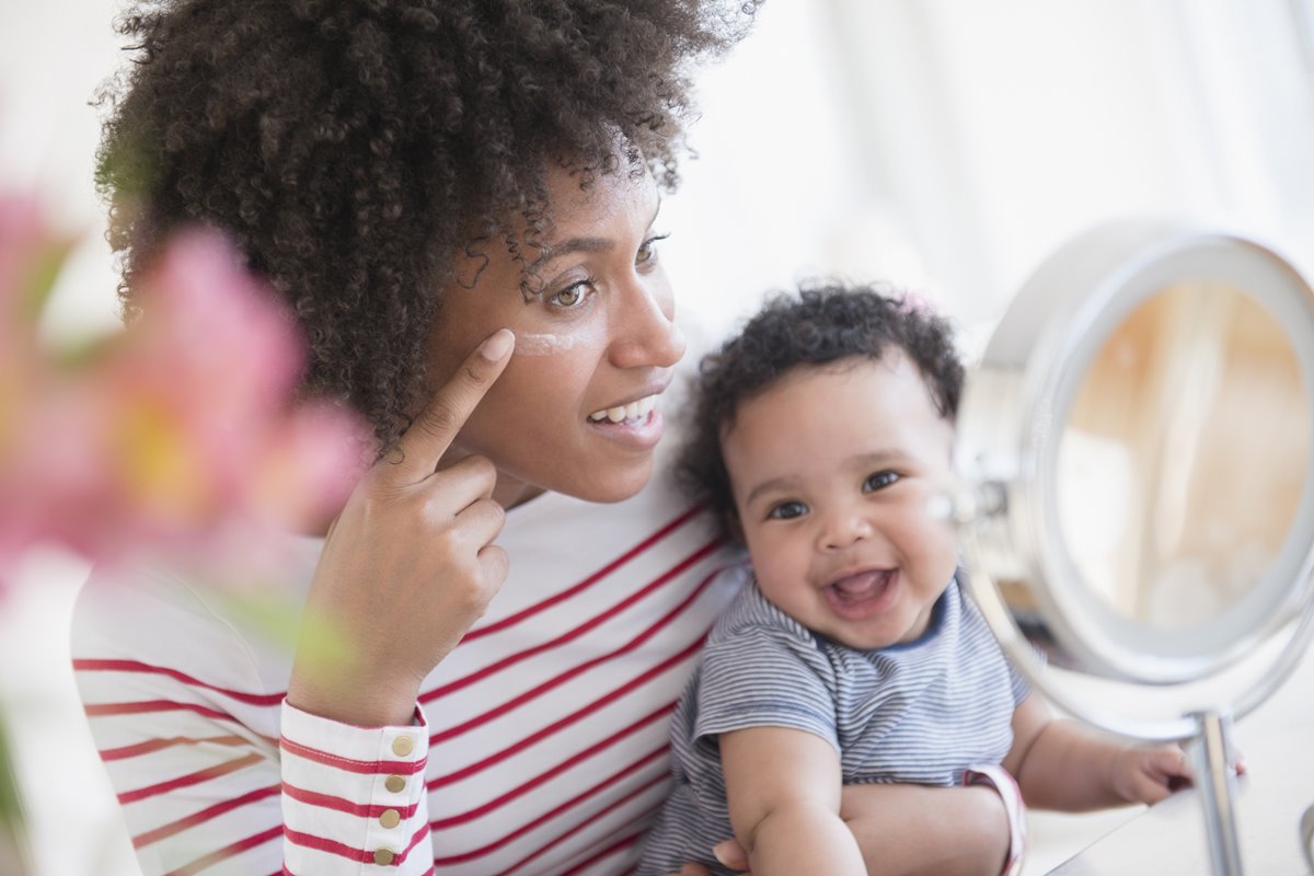 Mulher com bebê enquanto passa creme no rosto