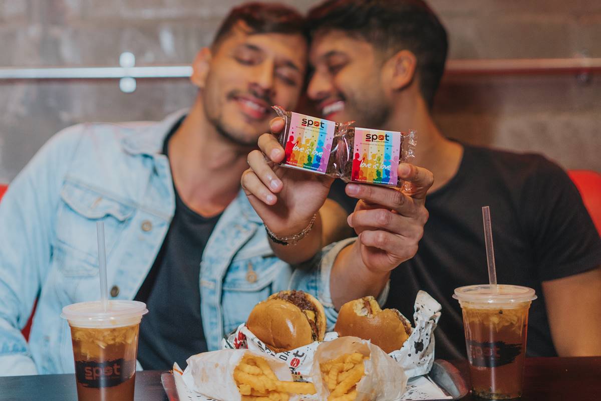 Dois homens sorriem e seguram brownies com embalagem de arco íris e frase LOVE IS LOVE