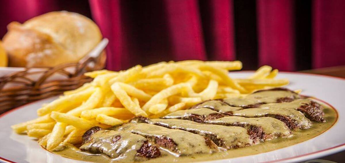 Prato com entrecote coberto de molho e batatas fritas