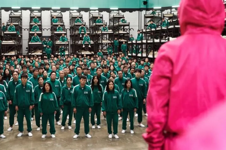 Foto com várias pessoas de macacão verde olhando para uma pessoa de macacão vermelho - Metrópoles