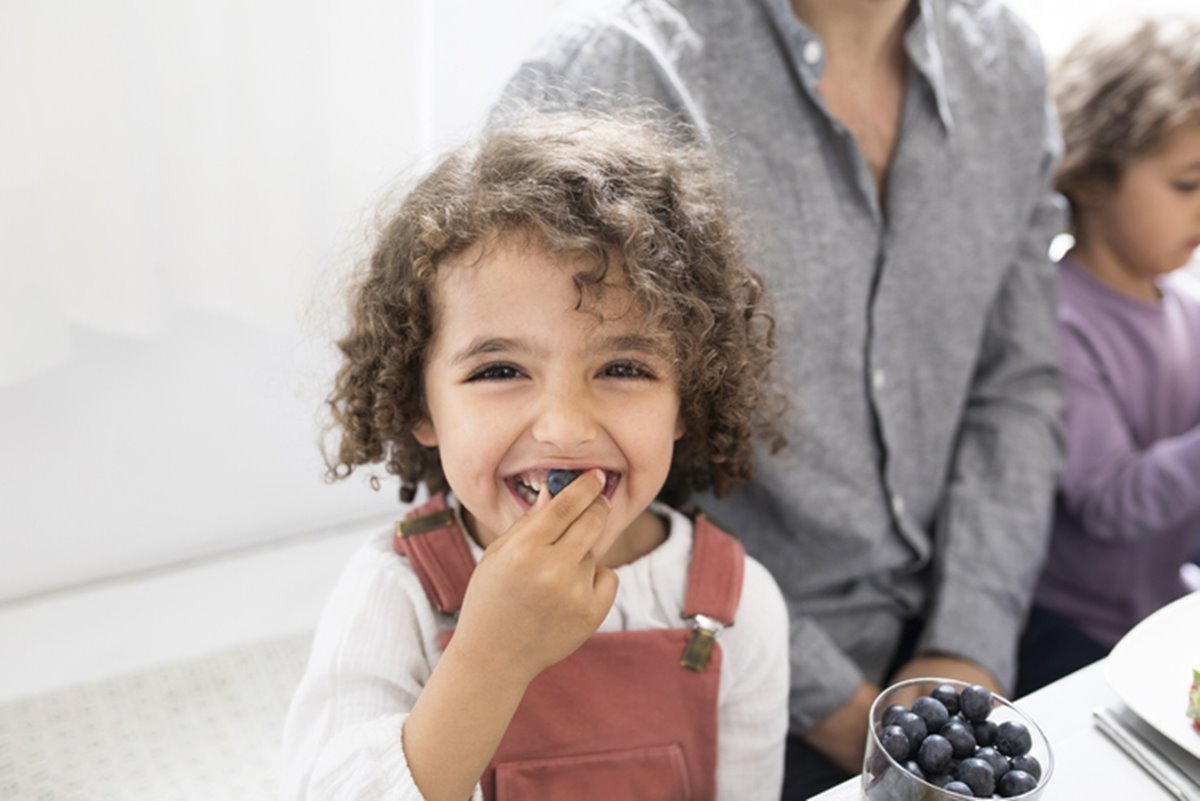 Na foto, criança branca com cabelo cacheado comendo fruta - Metrópoles