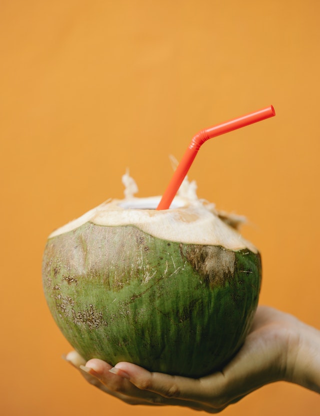 Mão segurando coco com canudo