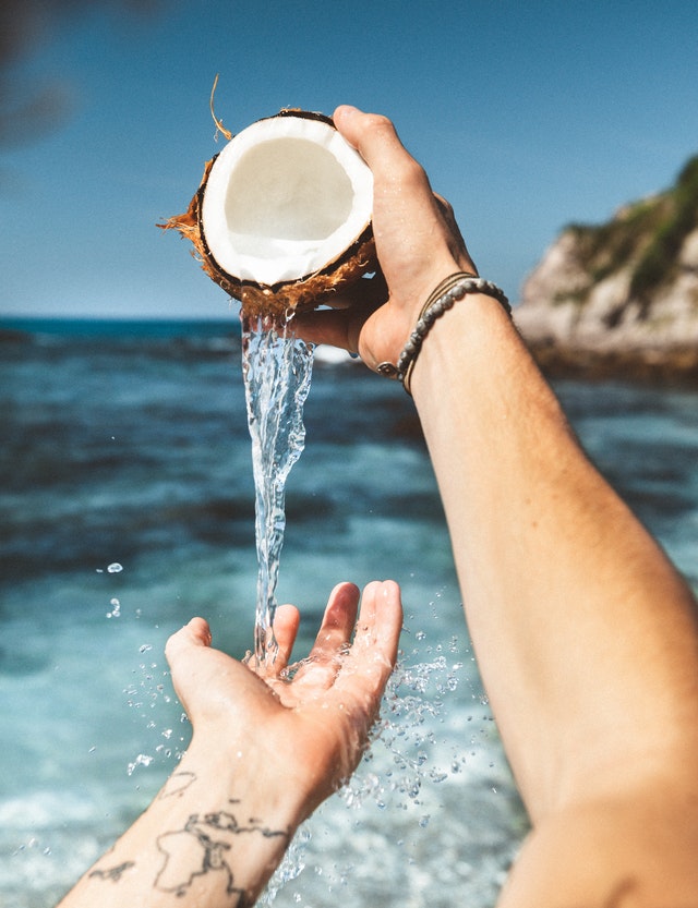 mãos segurando coco natural com mar ao fundo