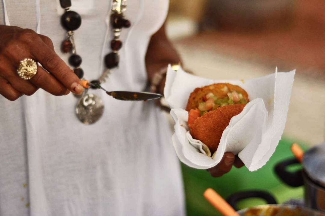 Na foto, uma baiana segura o acarajé enquanto recheia o bolinho