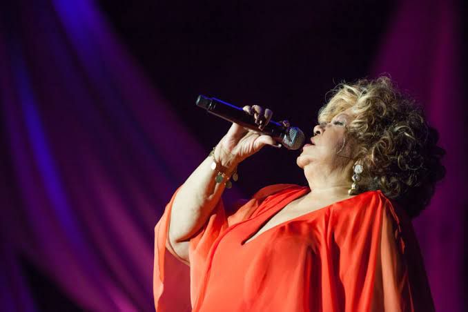 Foto colorida de Alcione cantando com roupa laranja - Metrópoles