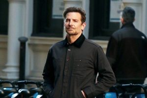 Bradley Cooper com casaco preto e mãos no bolso - Metrópoles