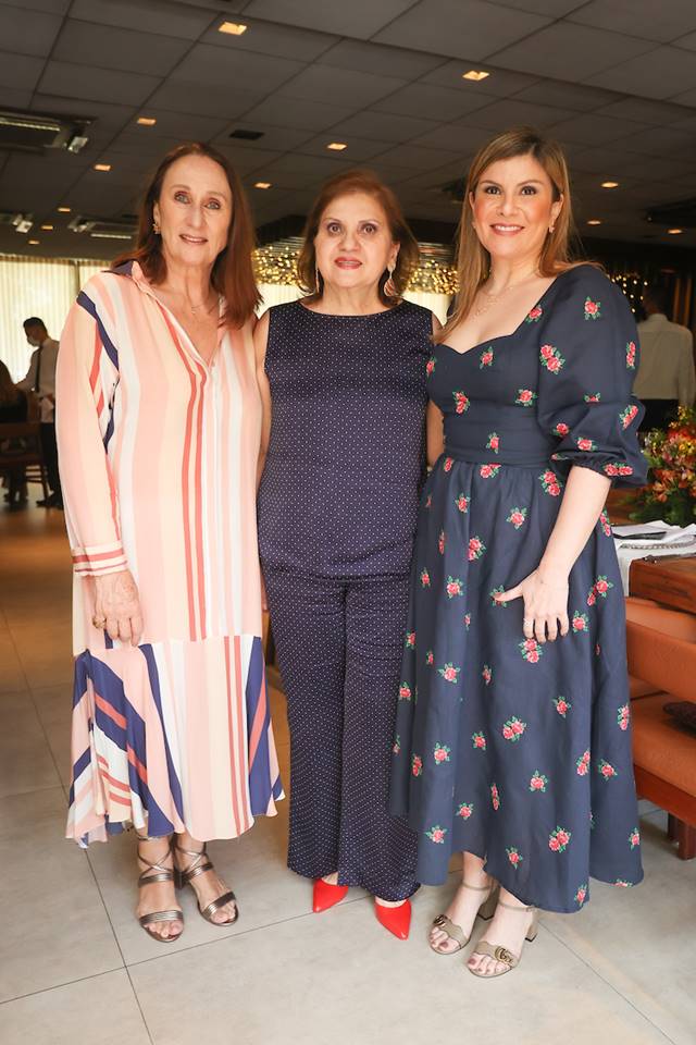 Três mulheres juntas com vestido estampado, um conjunto azul escuro e com vestido azul escuro