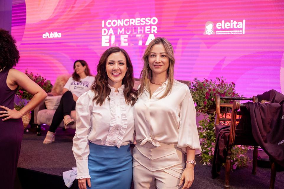 Mulheres abraçadas em frente a telão na cor rosa