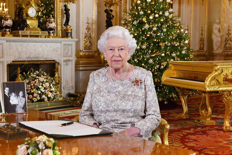 Mulher de cabelos brancos com árvore de Natal ao fundo, quadros e um piano. 