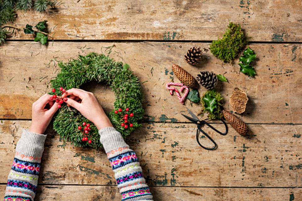 Uma pessoa montando uma guirlanda de natal com produtos naturais 