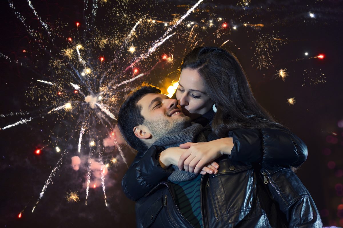 Casal se beijando. Ao fundo, fogos de artifício