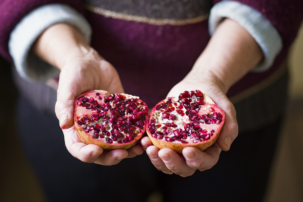 Mulher segura romã. A fruta está duvida ao meio