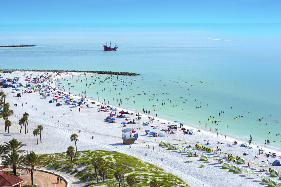 Praia com pessoas, coqueiros e barcos na areia