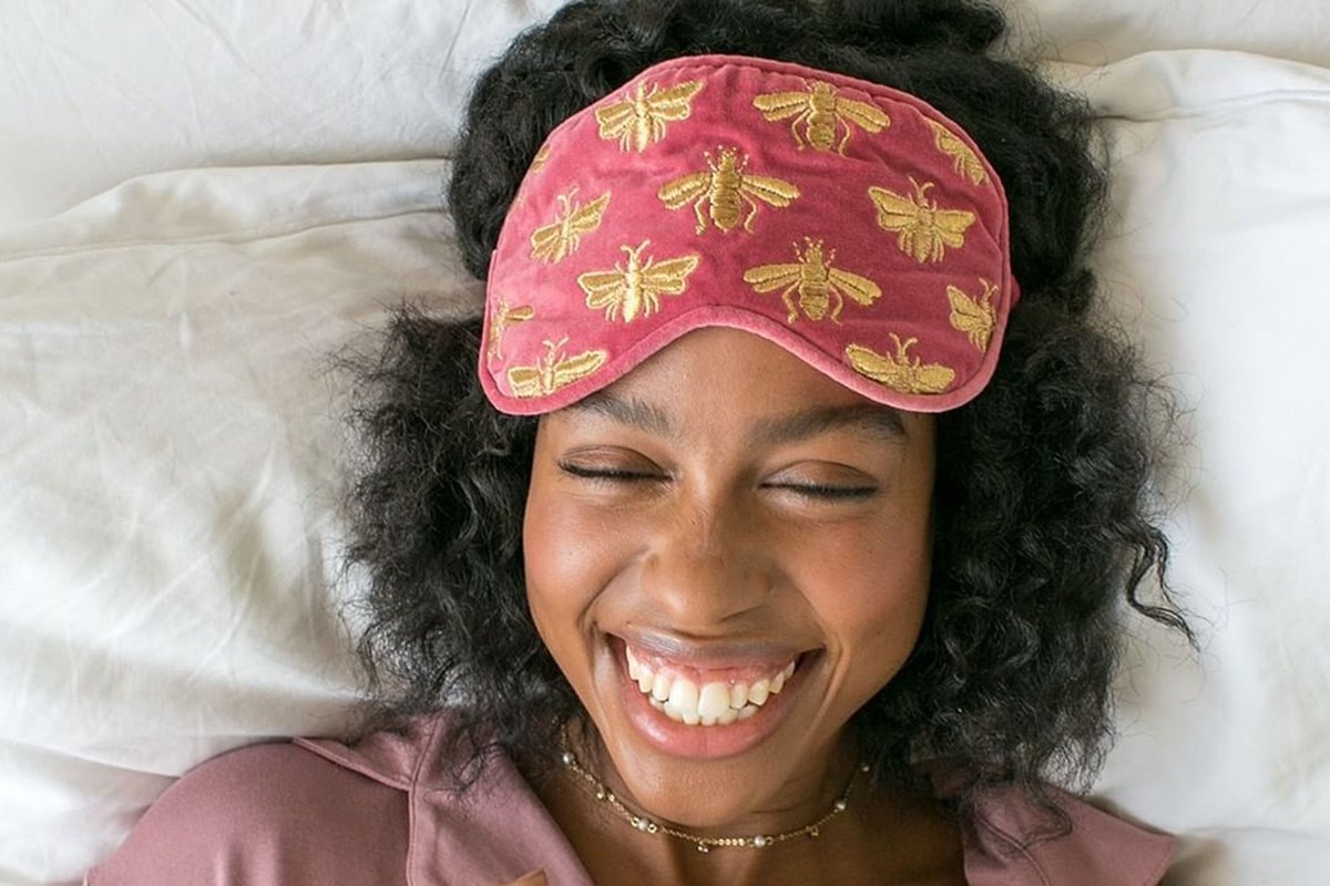 Mulher negra, sorridente, com um tapa olhos de estampa de abelhas na testa