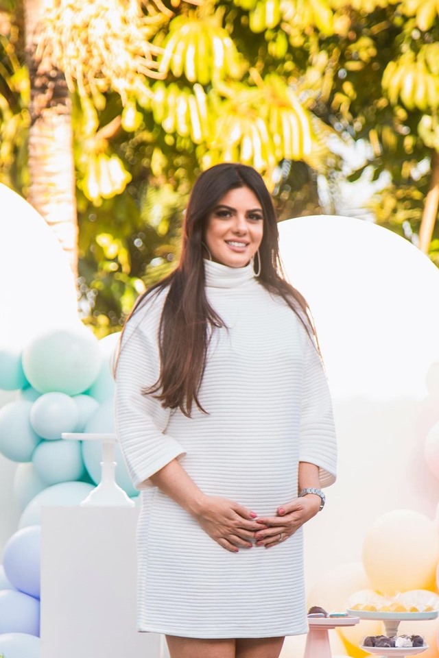 Mulher de cabelos longos com a mão na barriga. Ela está de vestido branco 