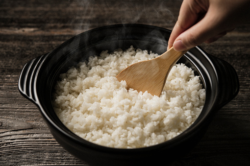 Arroz branco em uma tigela preta com uma mão segurando uma colher de pão