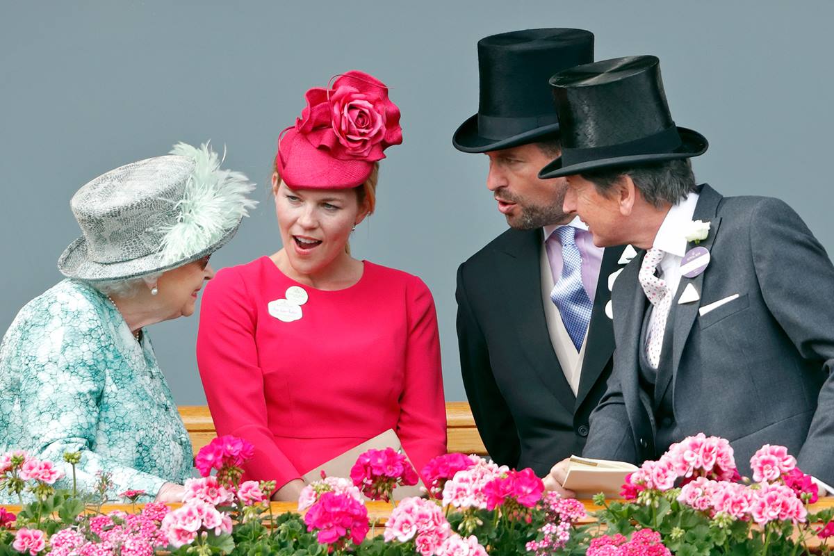 Mulher de roupa verde ao lado de mulher de roupa rosa. Dois homens com terno estão ao lado