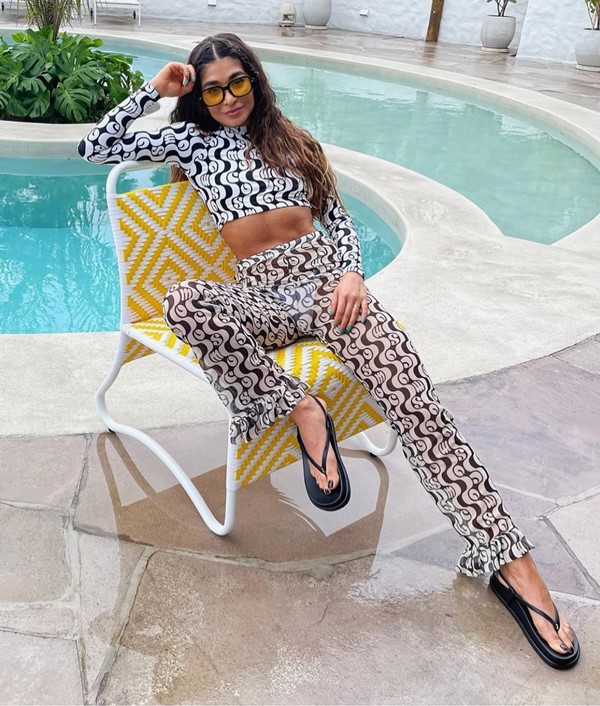 Mulher branca com cabelo castanho longo sentada em cadeira de tomar sol em frente à piscina