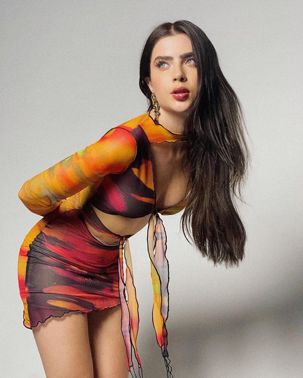 A influencer Jade Picon, do BBB22, posando em fundo branco com vestido vermelho e amarelo cheio de recortes