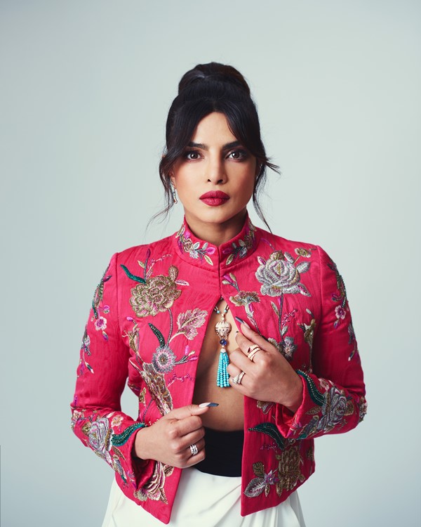 A atriz Priyanka Chopra Jonas em fundo branco com jaqueta rosa estampada e joias da marca Bulgari