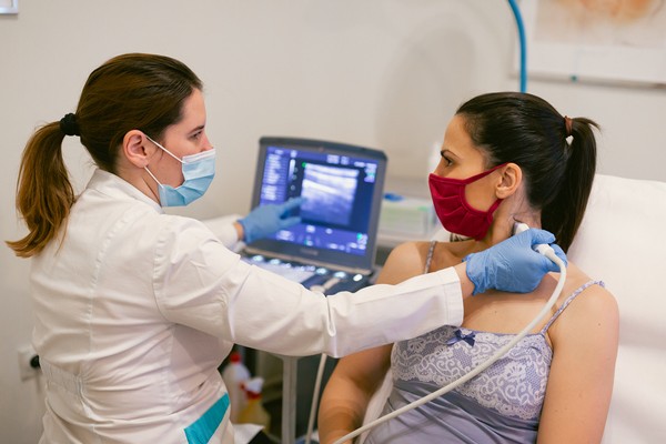 Mulher é examinada por médica na tireoide. Elas estão em consultório médico de máscara e sentadas, uma de frente pra outra-Metrópoles