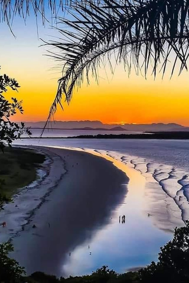 Foto de uma paisagem com pôr do sol, praia e árvores ao redor