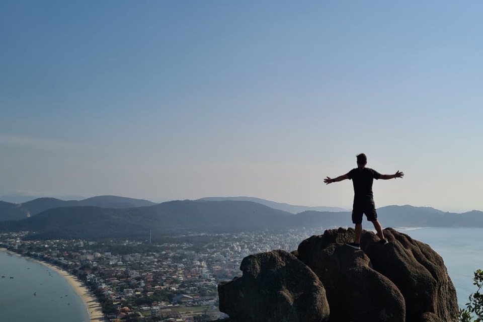 Homem em cima de uma rocha. Abaixo da imagem, há uma cidade 