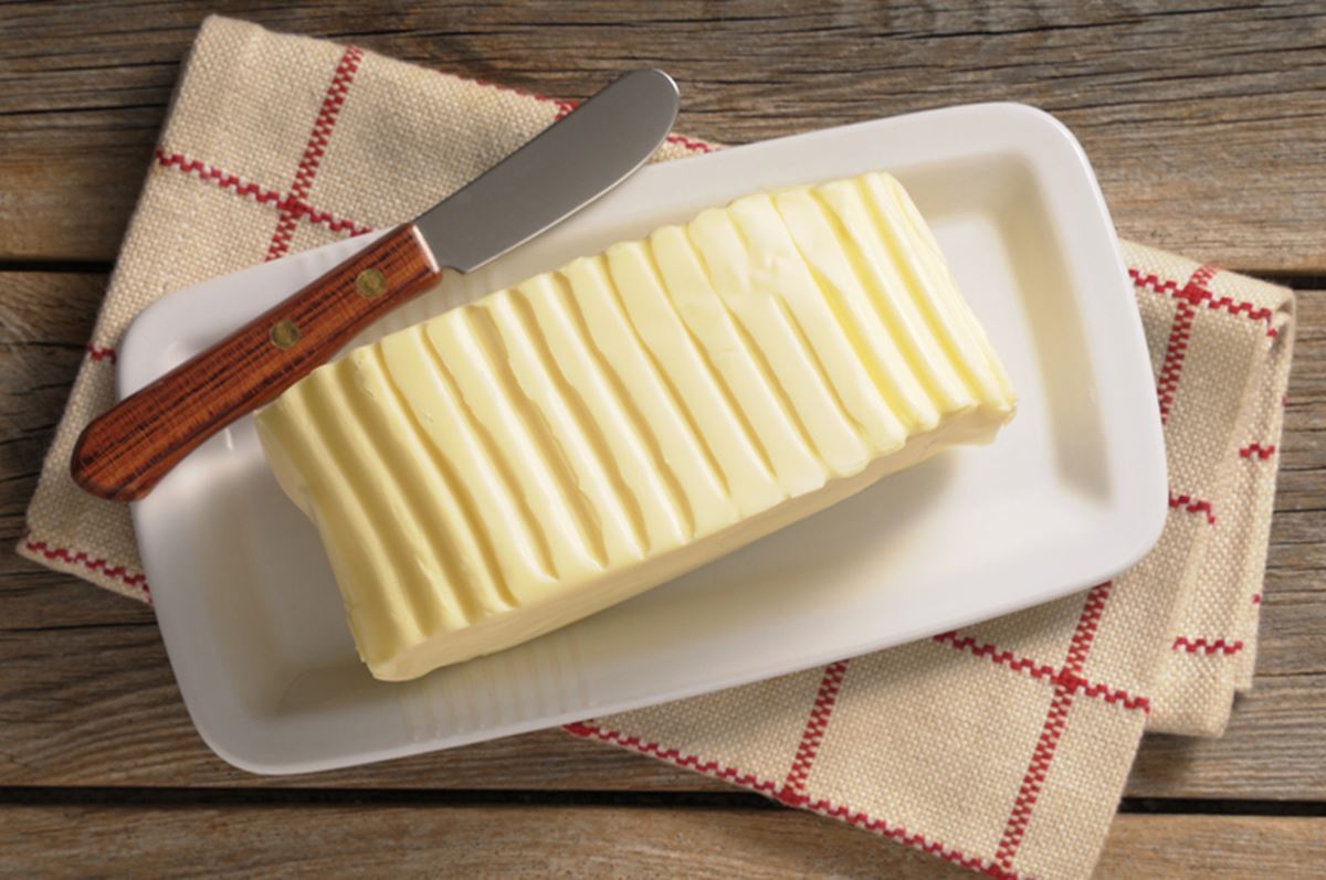 Na foto, um tablete amarelo de manteiga em cima de um recipiente branco - Metrópoles