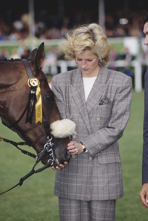 Mulher branca com blazer acariciando um cavalo