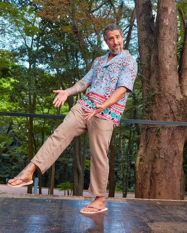 Marcos Mion, apresentador da Rede Globo, com camisa estampada e calça marrom. Ele usa chinelos rosas da Havaianas