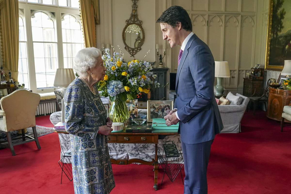 Foto colorida, Rainha Elizabeth com vestido estampado e Justin Trudeau com terno. Eles estão em uma sala