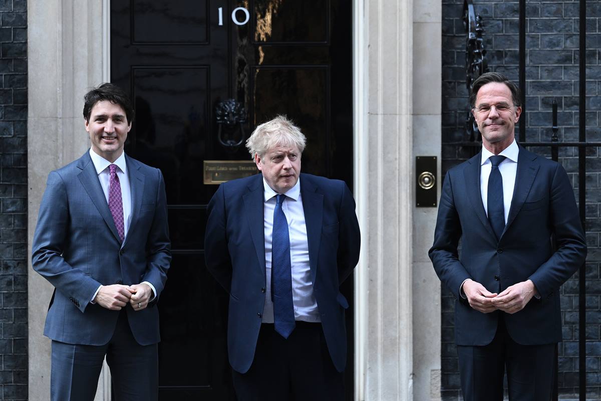 Foto colorida. Justin Trudeau, Boris Johnson e Mark Rutte de terno em frente a uma porta