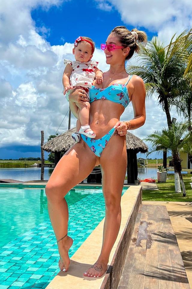 Foto colorida. Virginia Fonseca segura Maria Alice no colo perto de uma piscina 