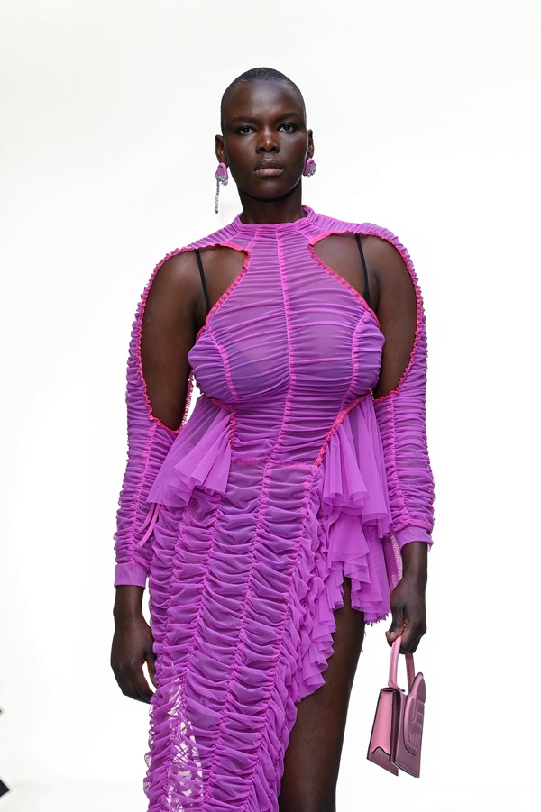 Mulher negra e careca usando vestido franzido roxo. Ela está desfilando pela marca Ester Manas.