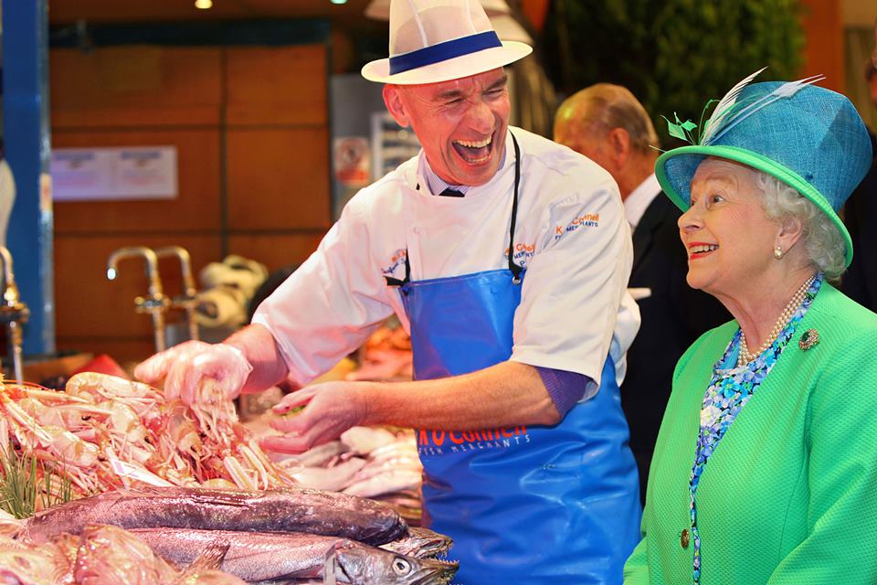 Foto colorida. Rainha Elizabeth ao lado de um homem e peixes