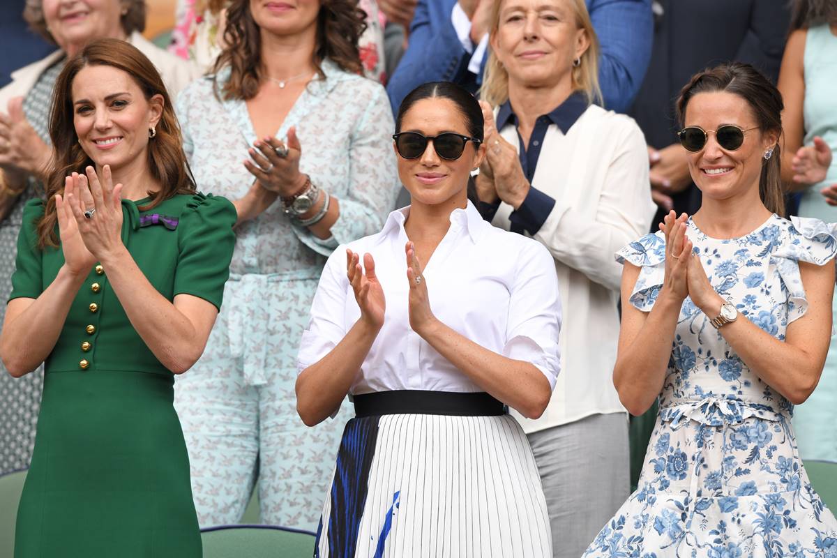 Foto colorida. Kate Middleton, Meghan Markle e Pippa Middleton em uma arquibancada