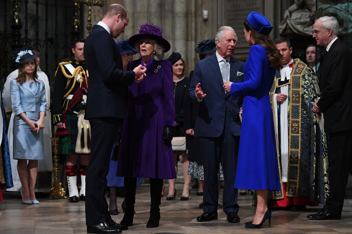 Foto colorida. Momento do encontro do príncipe William, Camilla Parker, príncipe Charles e Kate Middleton. Os príncipes vestem terno e as duquesas roupas azul e roxo