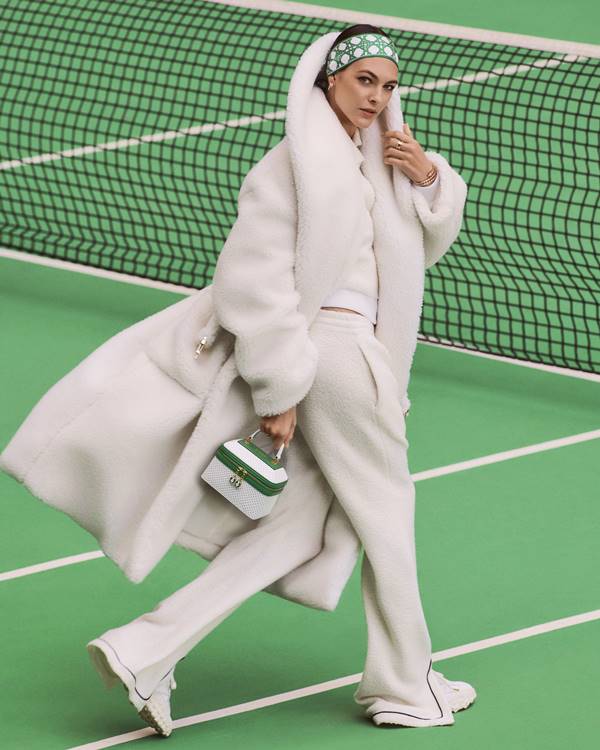 Modelo usando look branco e segurando bolsa branca com verde em quadra de tênis