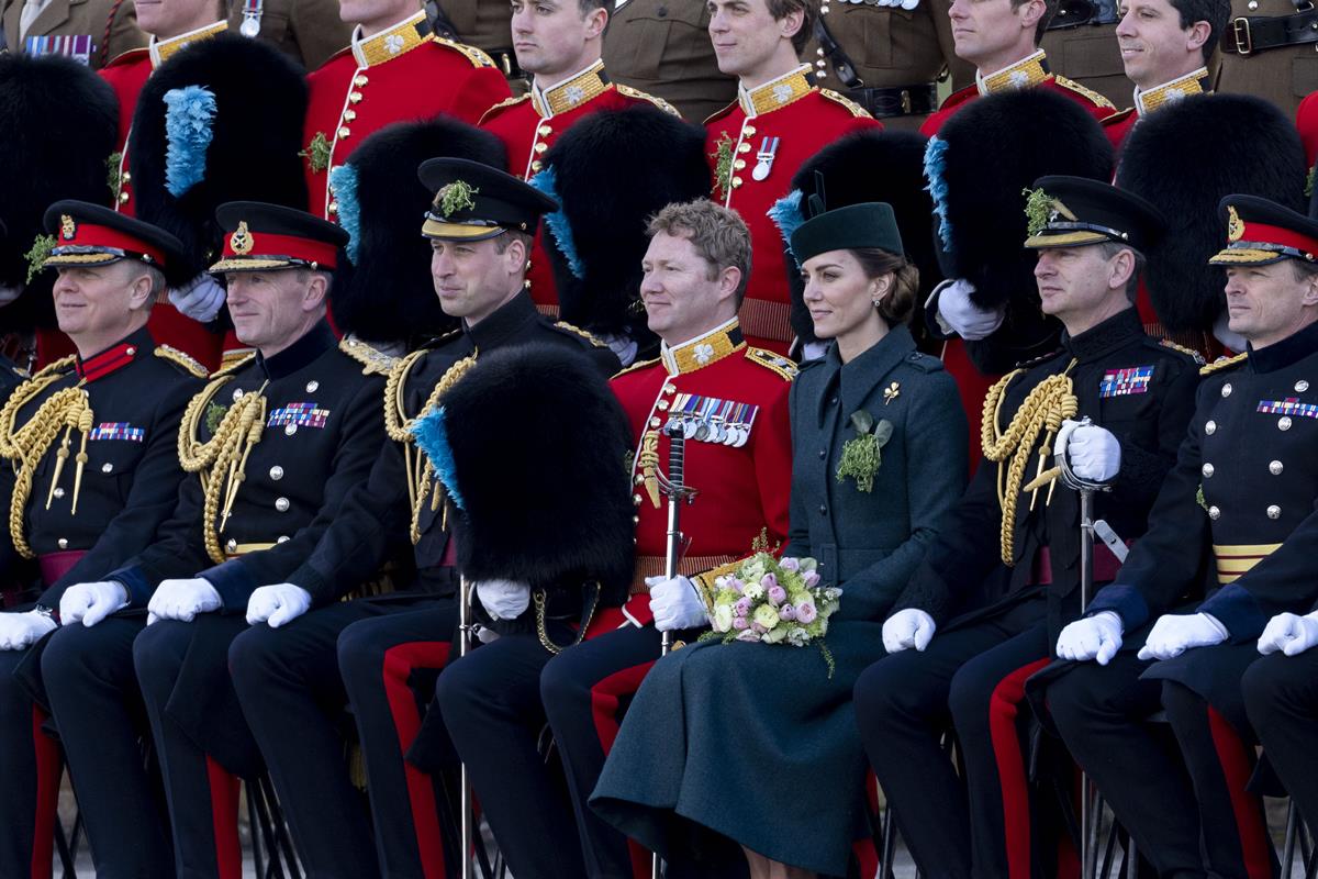 Foto colorida. Príncipe William e Kate Middleton entre oficiais britânicos