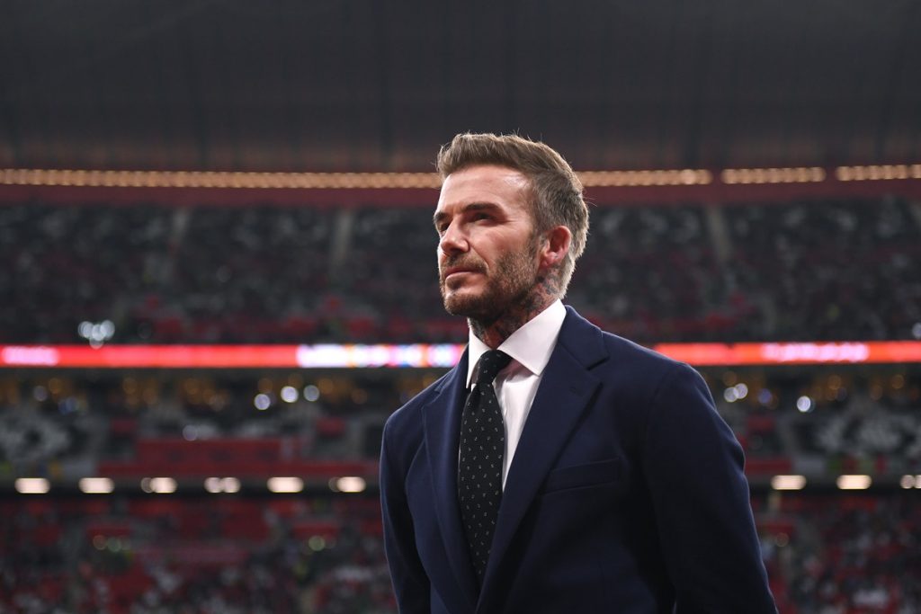 Foto colorida de David Beckham usando terno em estádio de futebol - Metrópoles