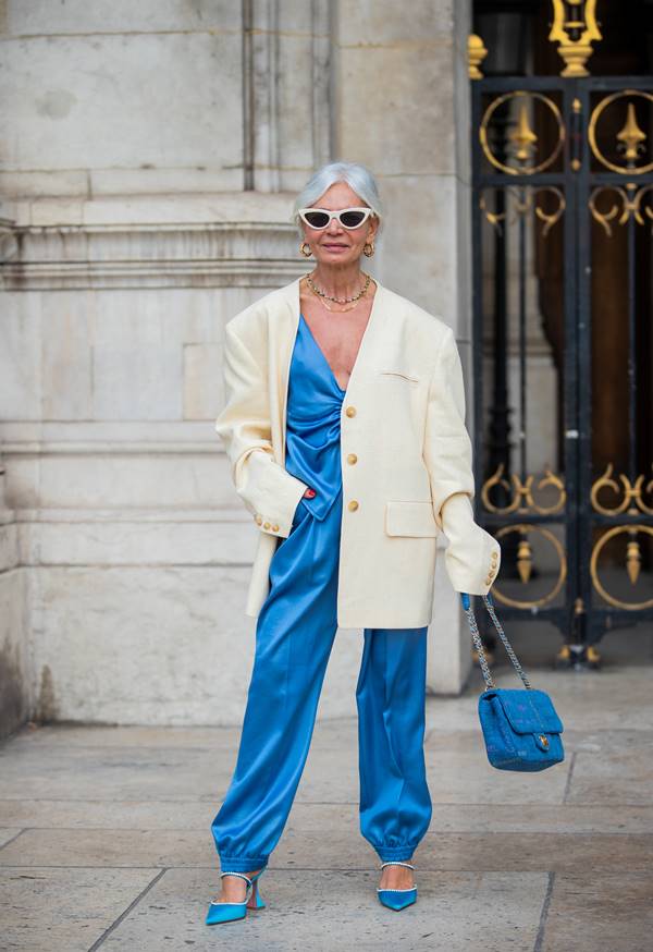 Look com macacão azul acetinado e blazer branco no street style