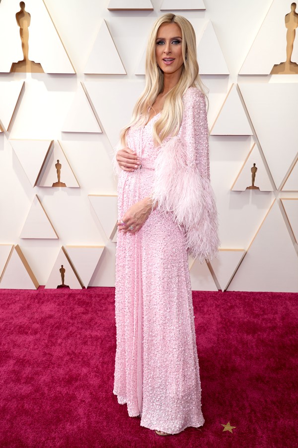 A socialite Nicky Hilton, irmã de Paris Hilton, no tapete vermelho do Oscar 2022. Ela usa um vestido rosa com penas.